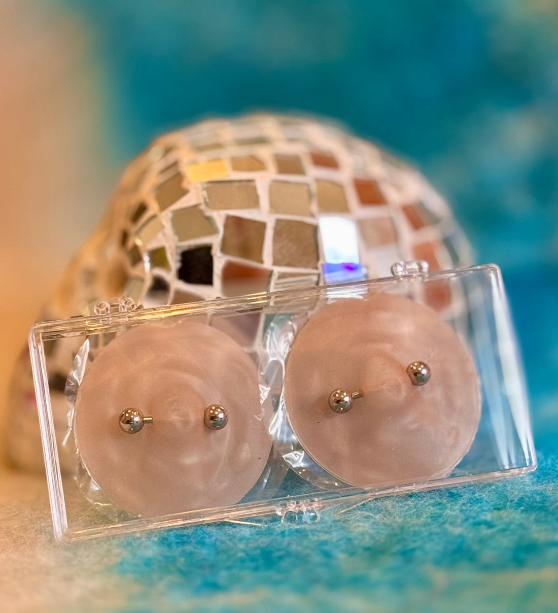 Nikkys Nips pierced pasties fashion placed on top of a blue background with a disco ball behind it