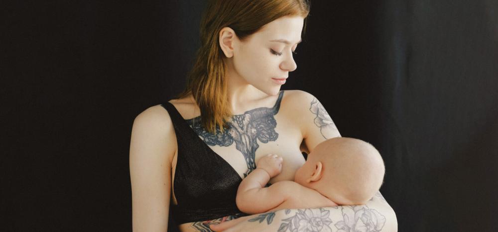 A tattooed mother breastfeeds her baby, with a black bra pulled aside.